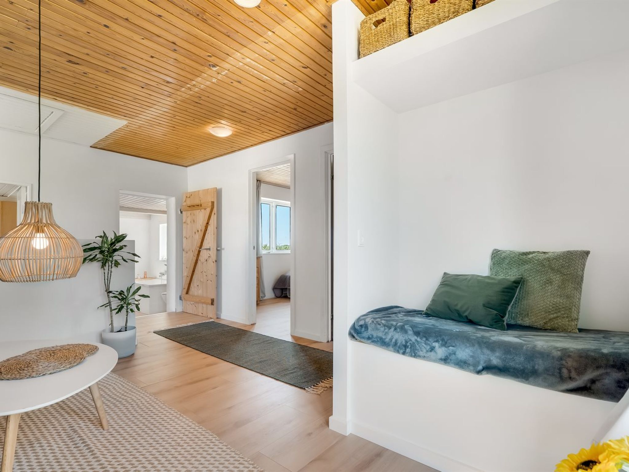 Un interior moderno con techo de madera, un sofá con cojines, una lámpara colgante y una planta en maceta.