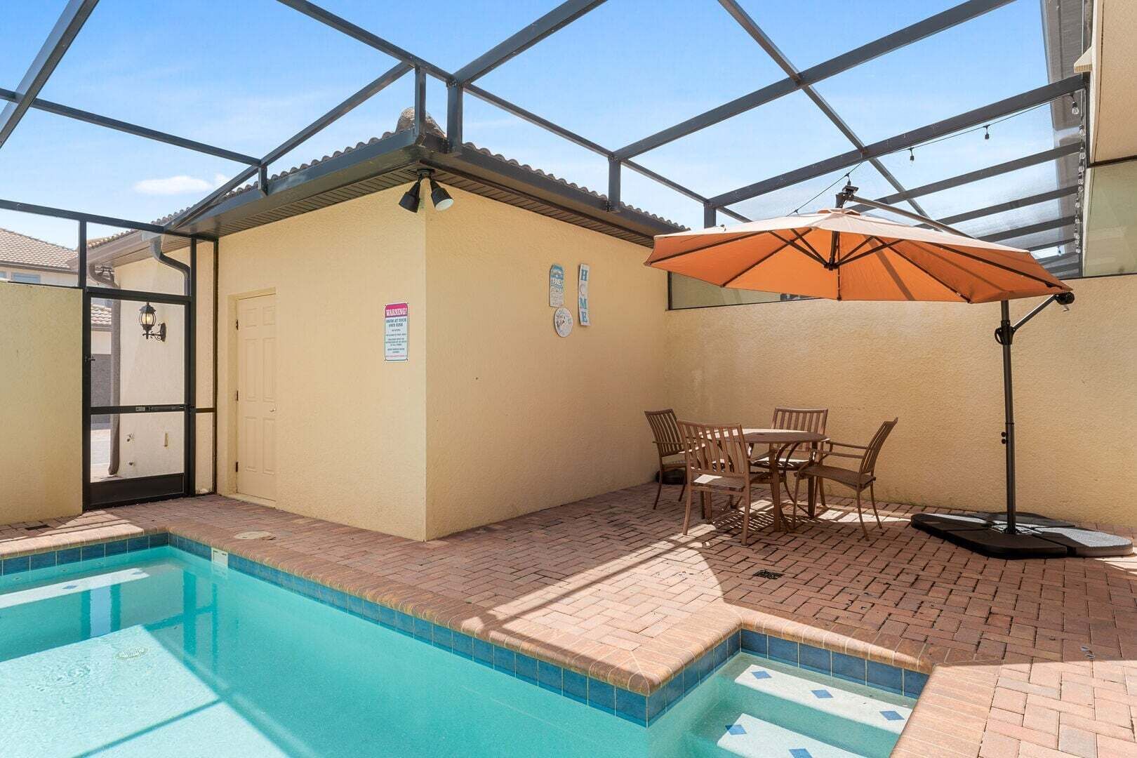 An indoor swimming pool with a glass ceiling, a poolside table with chairs, and an umbrella.