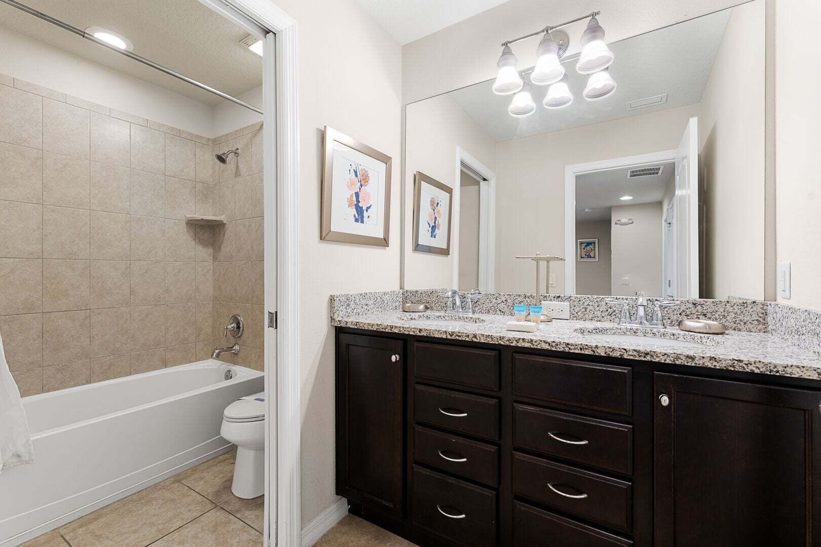 A bathroom with a bathtub, toilet, vanity with dark cabinets, and a large mirror.