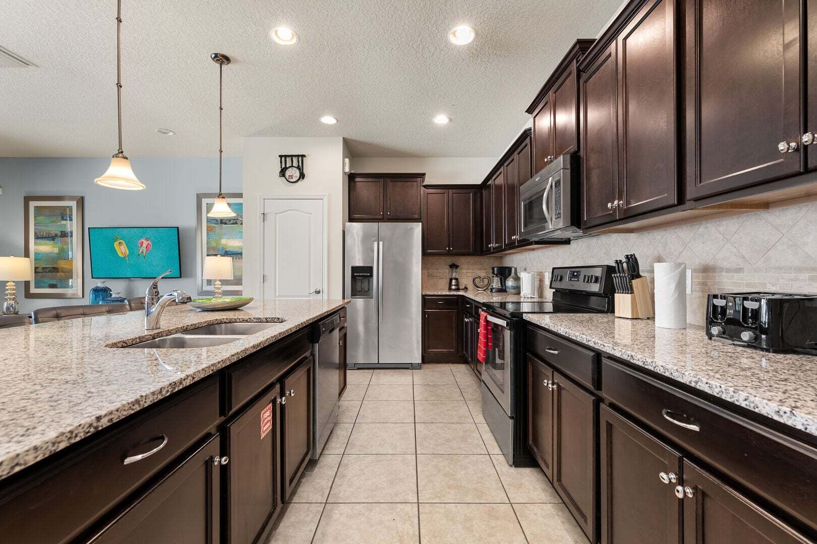 A modern kitchen with dark wood cabinets, granite countertops, stainless steel appliances, and pendant lighting.