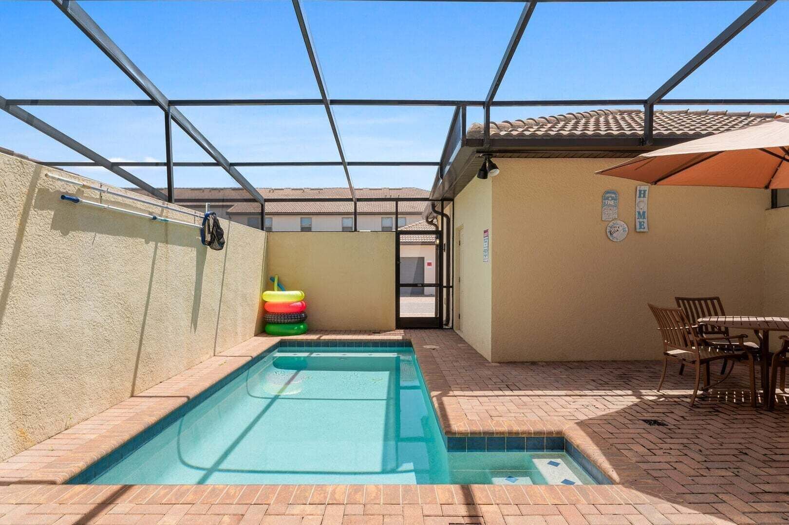 Une piscine entourée de parois en verre, une porte donnant accès à un bâtiment et une table avec des chaises.