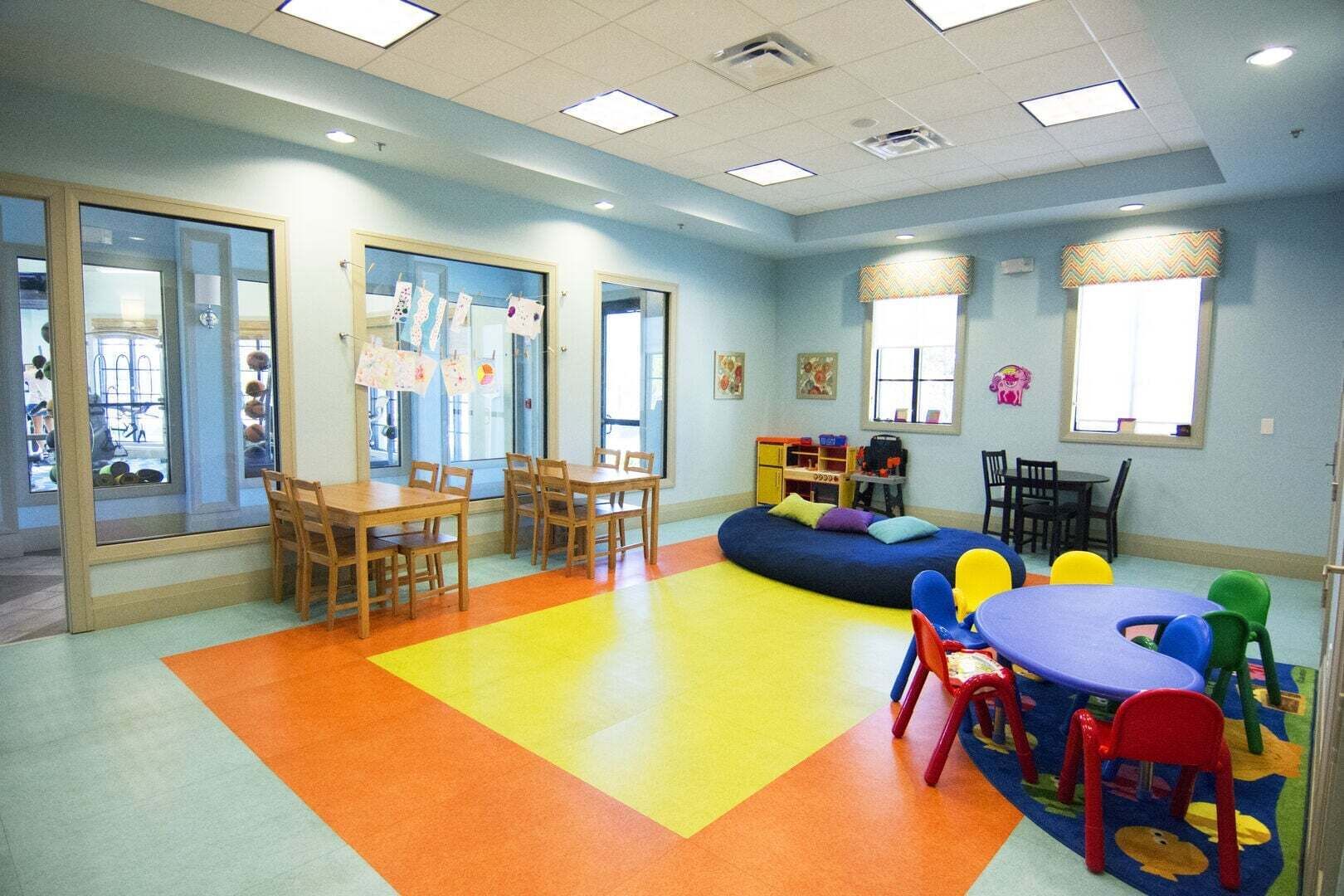 A children's playroom with a large table, chairs, a bean bag, and colorful play mats.