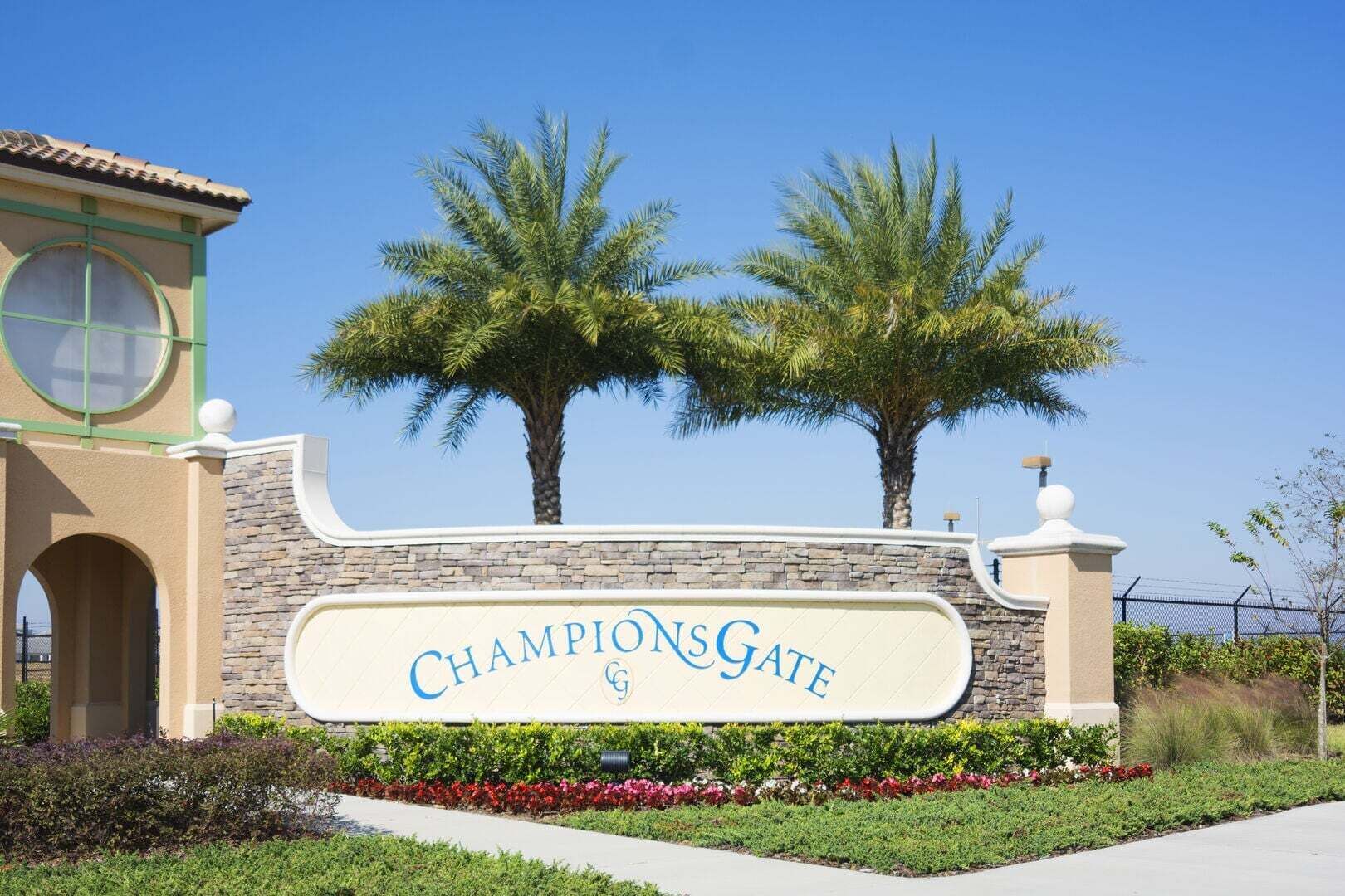Un panneau indiquant l’entrée de ChampionsGate, avec un mur de pierres, des palmiers et un ciel bleu dégagé.