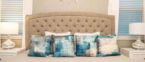 A bedroom with a tufted headboard, a bed with four pillows, a wall clock, and two bedside tables with lamps.
