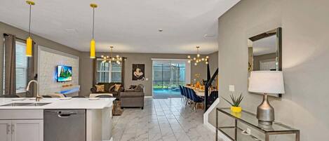 A modern kitchen with a built-in dishwasher, a dining area with a glass table, and a living room with a sofa and TV.
