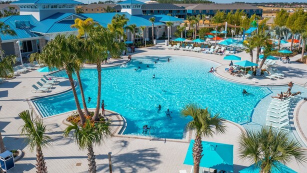 A large outdoor swimming pool surrounded by palm trees and lounge chairs, with a view of hotel buildings in the background. - Fun & Elegant w Pool, Cinema & Game Room (Davenport)