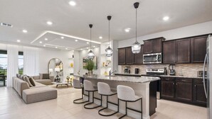 A modern kitchen with dark wood cabinets, stainless steel appliances, and a central island with bar stools. - Fun & Elegant w Pool, Cinema & Game Room (Davenport)