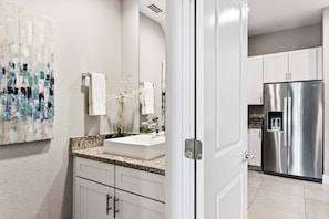 A modern kitchen with white cabinets, a stainless steel refrigerator, and a granite countertop. - Spacious Family Villa 5min to Disney (Kissimmee)