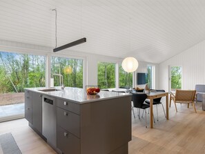 Eine moderne Küche mit einer großen Kochinsel, einem Essbereich mit Tisch und Stühlen sowie großen Fenstern mit Blick ins Freie.