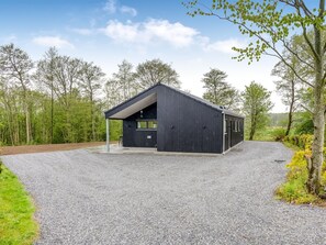 Ein modernes Gebäude mit geneigtem Dach, einer Schotterauffahrt und umgebendem Wald.