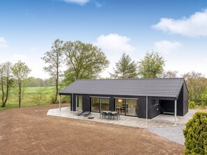 Ein modernes Haus mit einer großen Terrasse, großen Fenstern und Blick auf die umliegende Landschaft.