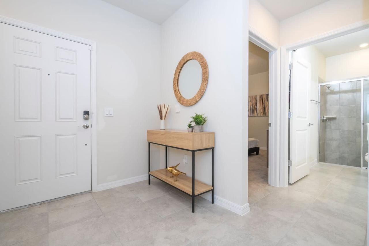 A hallway with a white door, a console table with a mirror, and a shower area.