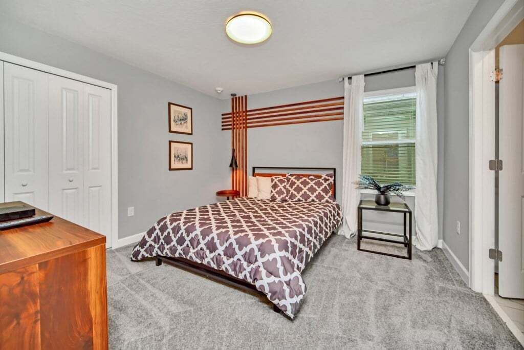 Une chambre à coucher comprenant un lit, un bureau, une chaise, une fenêtre avec des stores et une porte.