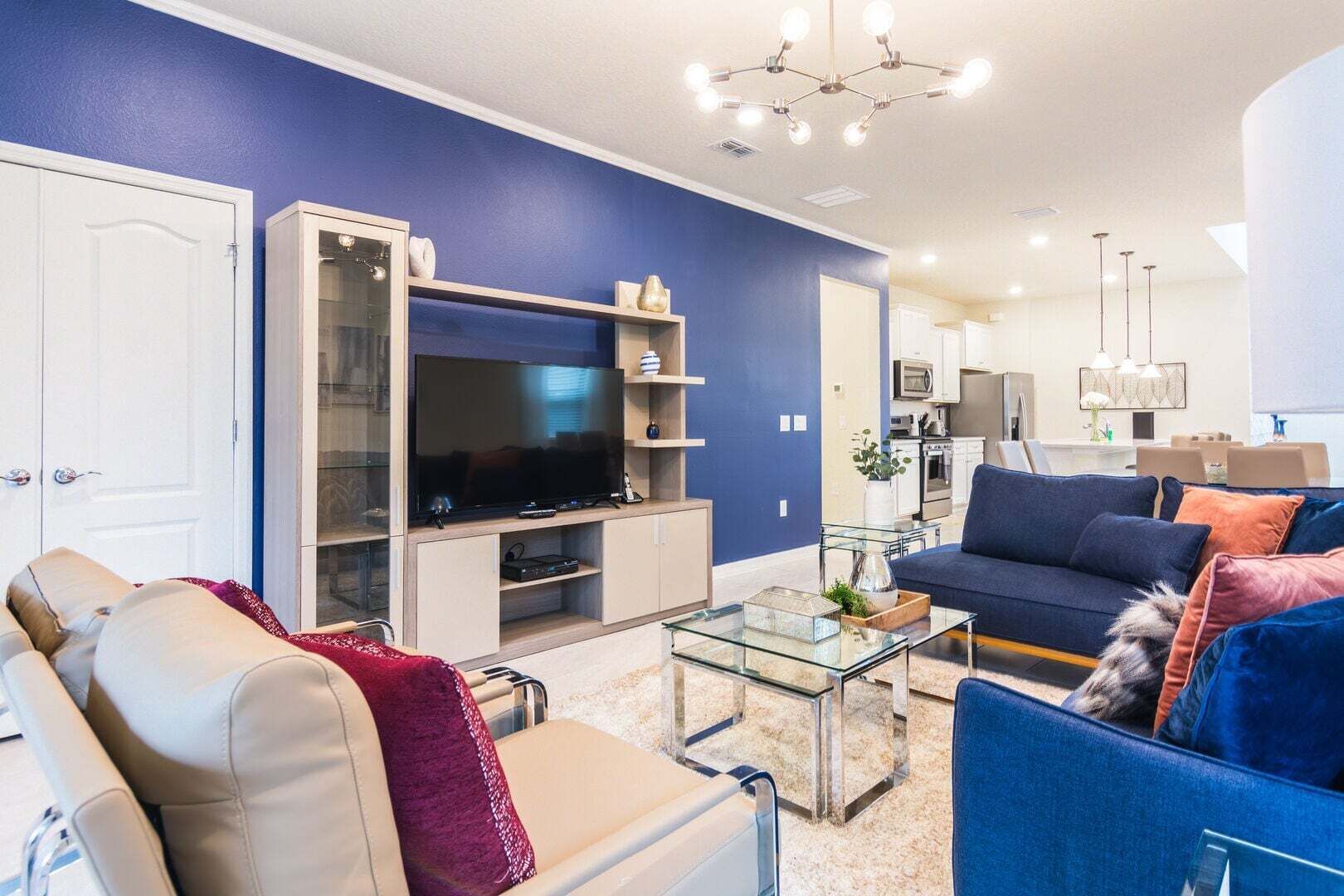 Sala de estar com televisão, sofá, mesa de centro e cozinha ao fundo.