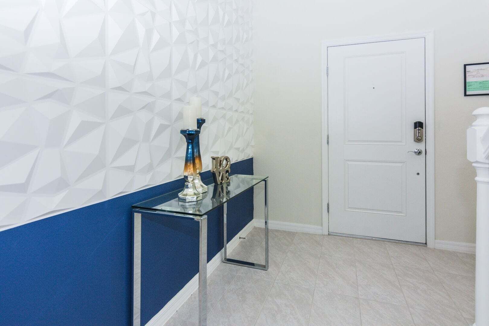A hallway with a geometric patterned wall, a white door, and a glass console table with decorative items.