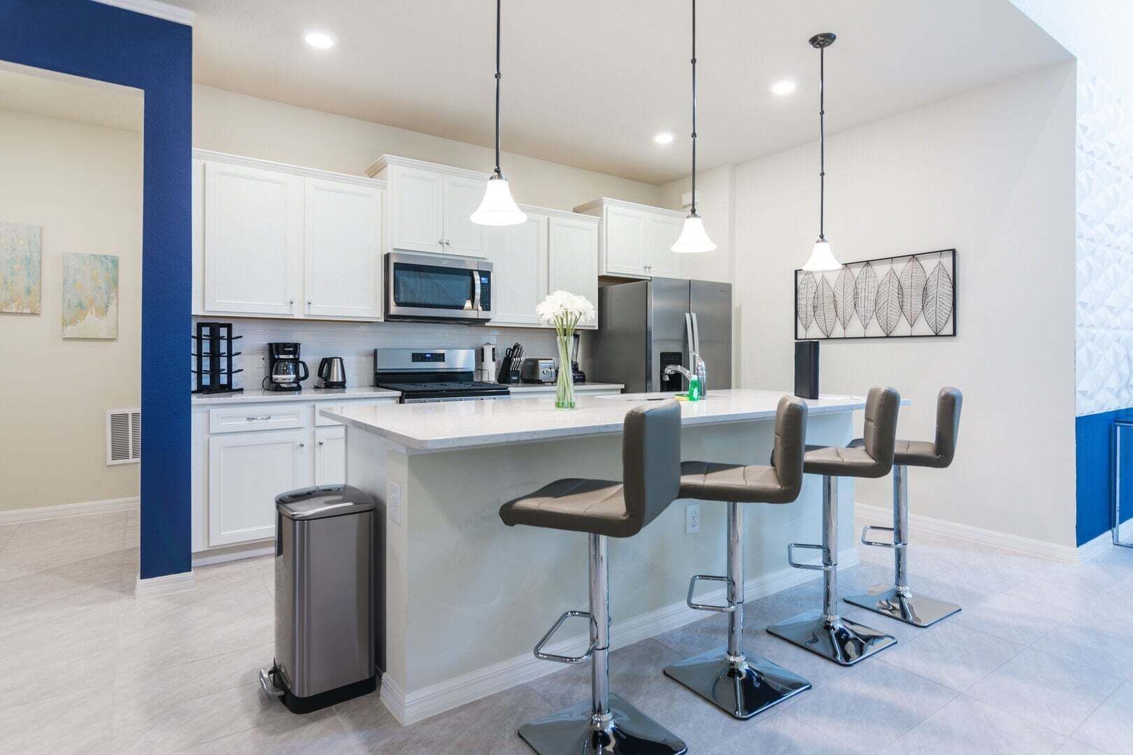 A modern kitchen with white cabinets, stainless steel appliances, and three bar stools.