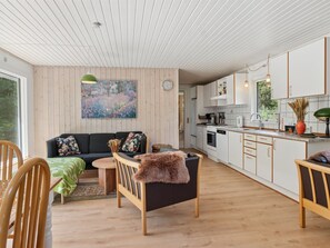 Ein modernes Interieur mit einer Couch, einem Esstisch, Stühlen, einer Küchenzeile und einem großen Fenster.
