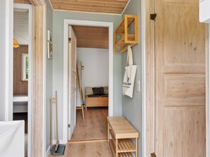 Ein Zimmer mit einem Bett, einer Holzbank, einem Besen und einem an der Wand befestigten Regal mit einer Tasche.