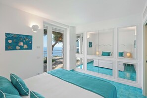 Ein Schlafzimmer mit Bett, ein Badezimmer mit Spiegel und Blick auf das Meer.