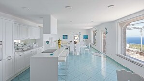 Una cocina moderna con armarios blancos, una isla central y vistas al mar a través de amplios ventanales.
