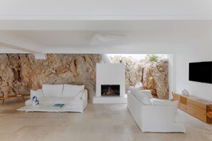 A modern living room with a stone wall, a fireplace, and a flat-screen TV. - Villa Vento Blu, Exclusive Luxury in Capri (Anacapri)
