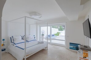 A modern bedroom with a four-poster bed, a TV, and a view of the outdoor area. - Villa Vento Blu, Exclusive Luxury in Capri (Anacapri)