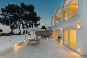 A modern outdoor patio with a dining area, white furniture, and a stone wall. - Villa Vento Blu, Exclusive Luxury in Capri (Anacapri)