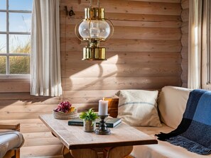 A cozy cabin interior with a wooden wall, a table with a candle, a book, and a bowl of grapes. - "Apelone" - 450m from the sea by Interhome (Blokhus)