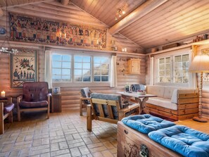 Ein Blockhaus-Interieur mit einer hölzernen Bank, einer gepolsterten Couch, einem Esstisch und einem Kamin.