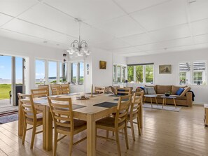 A spacious room with a wooden dining table and chairs, a sofa, and large windows offering a view of the outdoors. - "Elodie" - 10m from the sea by Interhome (Bjert)