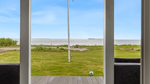 Um mastro de bandeira numa área ajardinada, com vista para um corpo de água e terra ao longe.