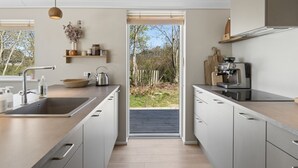 Une cuisine moderne dotée d’un grand îlot central, d’appareils électroménagers intégrés et offrant une vue sur l’extérieur.