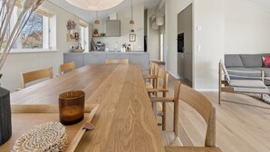 Une cuisine moderne dotée d’une grande table en bois, d’appareils électroménagers intégrés et de luminaires suspendus.