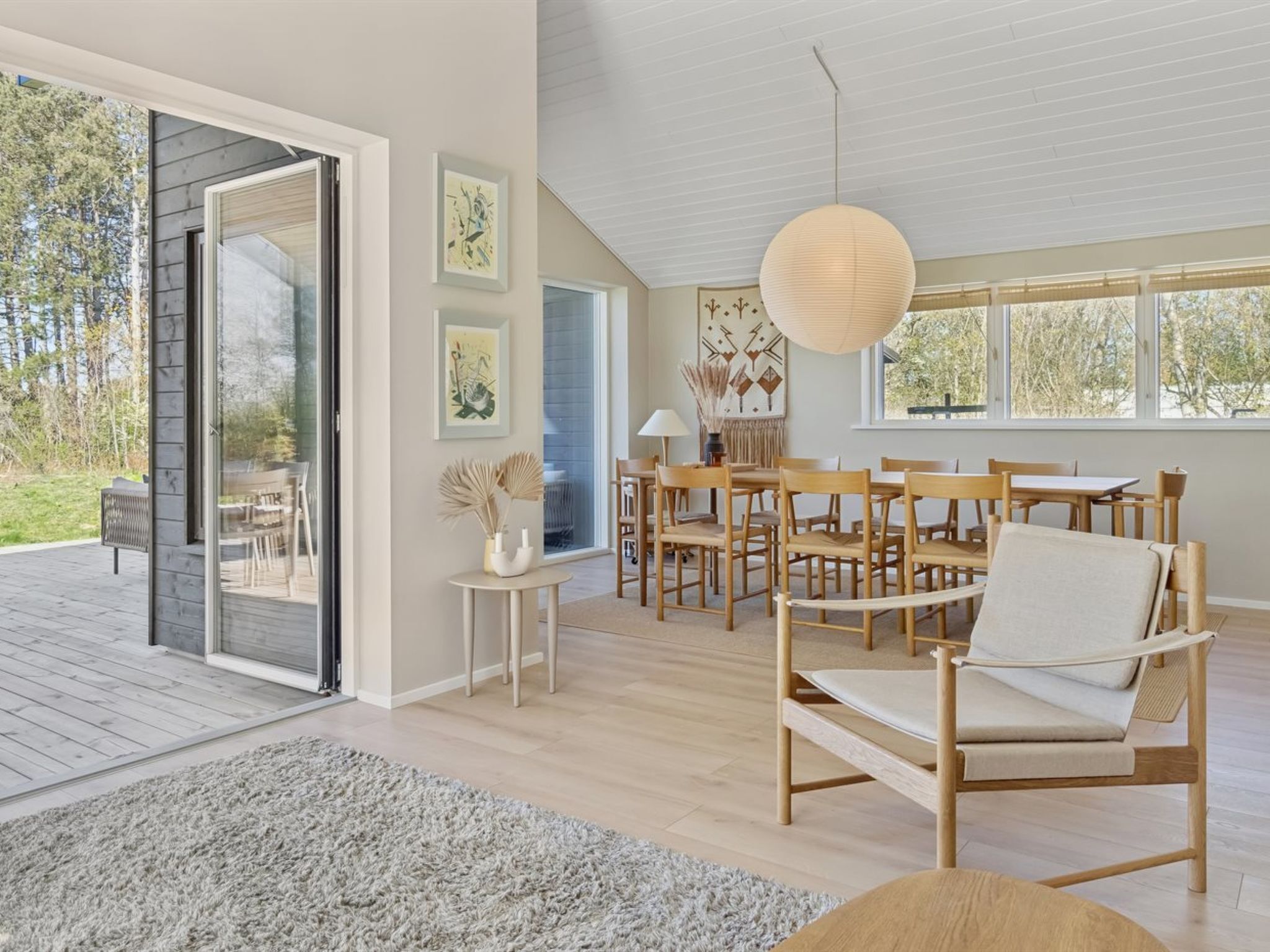 A spacious room with a large sliding glass door leading to an outdoor area, a dining area with wooden furniture, and a large paper lantern hanging from the ceiling.