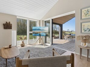 Een moderne woonkamer met een grote televisie, een houten tafel, een bank en uitzicht op een terras en buitenruimte.