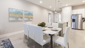 A modern kitchen with stainless steel appliances, a dining area with white chairs, and two abstract paintings on the wall. - Fantastic Townhome 5min-disneyworld 134 (Kissimmee)