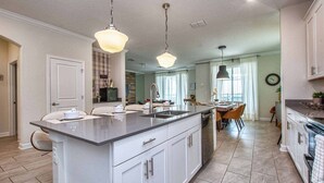A modern kitchen with a central island, pendant lighting, and a dining area with a view. - Fancy Family Home 10min-disney Private Pool 108 (Kissimmee)