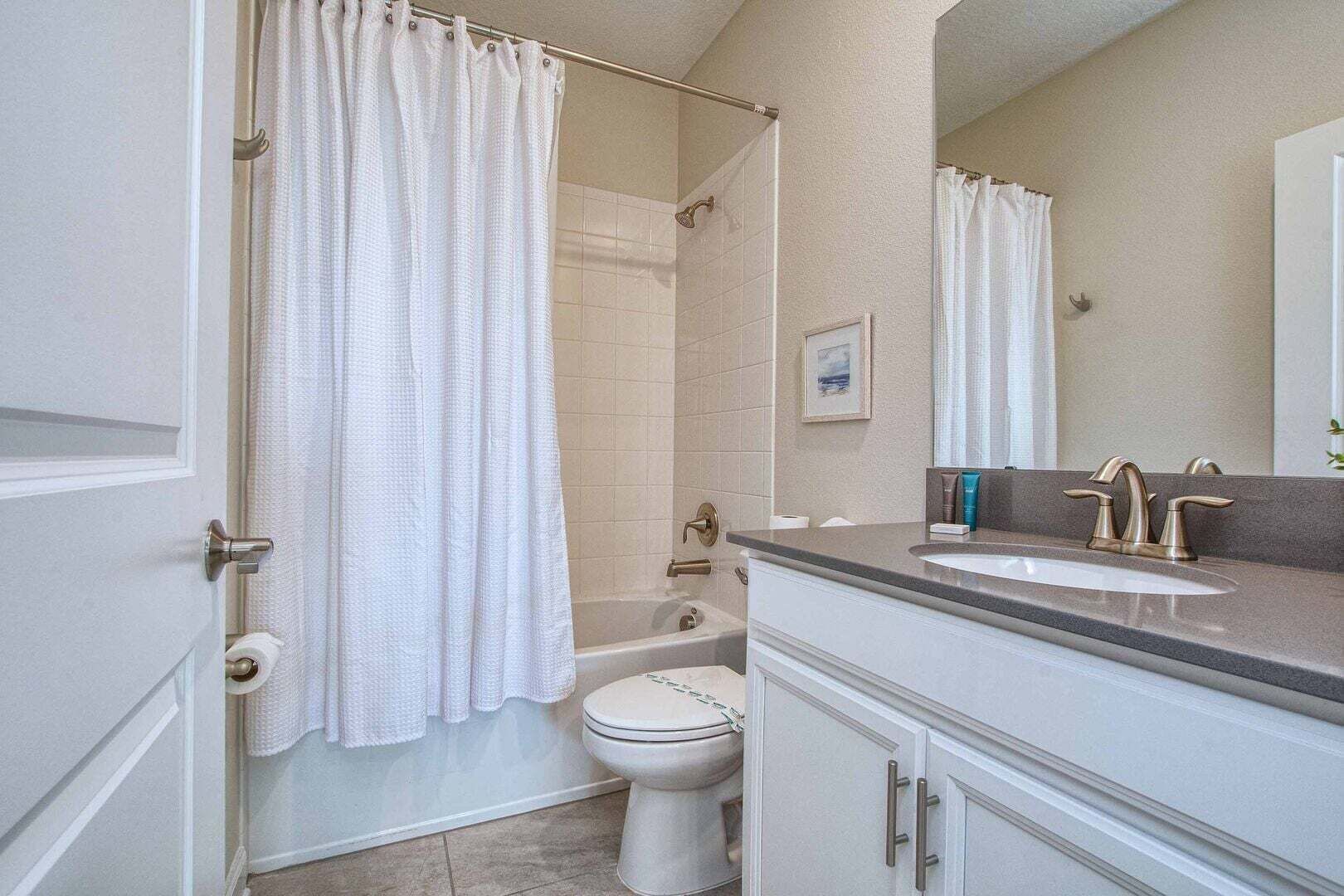 Ein Badezimmer mit Duschvorhang, Toilette, Waschbecken mit Spiegel und Handtuchhalter.