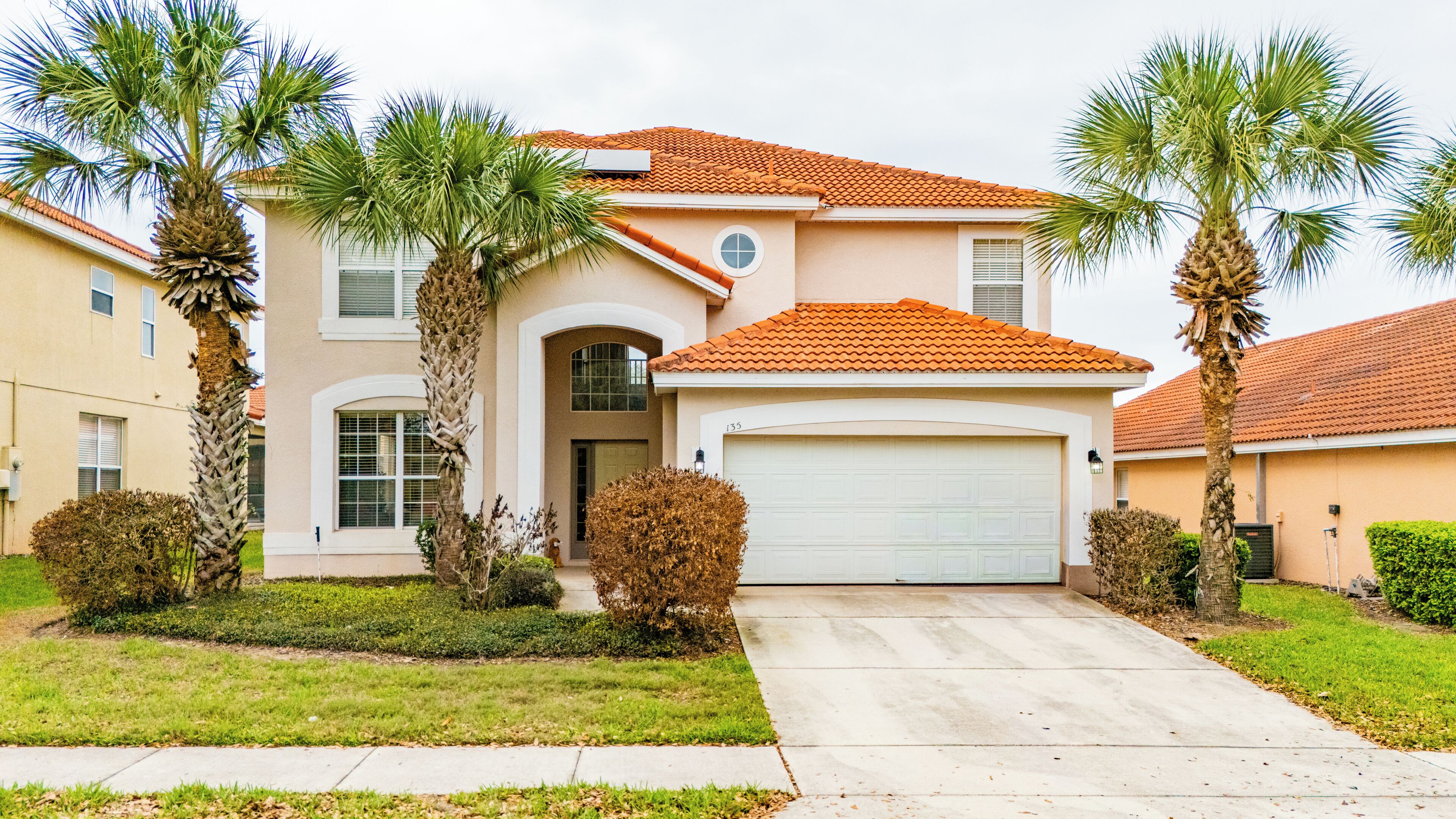A two-story house with a garage, palm trees, and a well-maintained lawn.