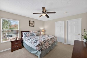 A bedroom with a bed, a nightstand, a ceiling fan, a window with blinds, and a door. - Family Getaway: 6BR w/ Private Pool & Resort Access (Davenport)