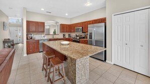 A modern kitchen with granite countertops, wooden cabinets, stainless steel appliances, and a large island with bar stools. - Family Getaway: 6BR w/ Private Pool & Resort Access (Davenport)