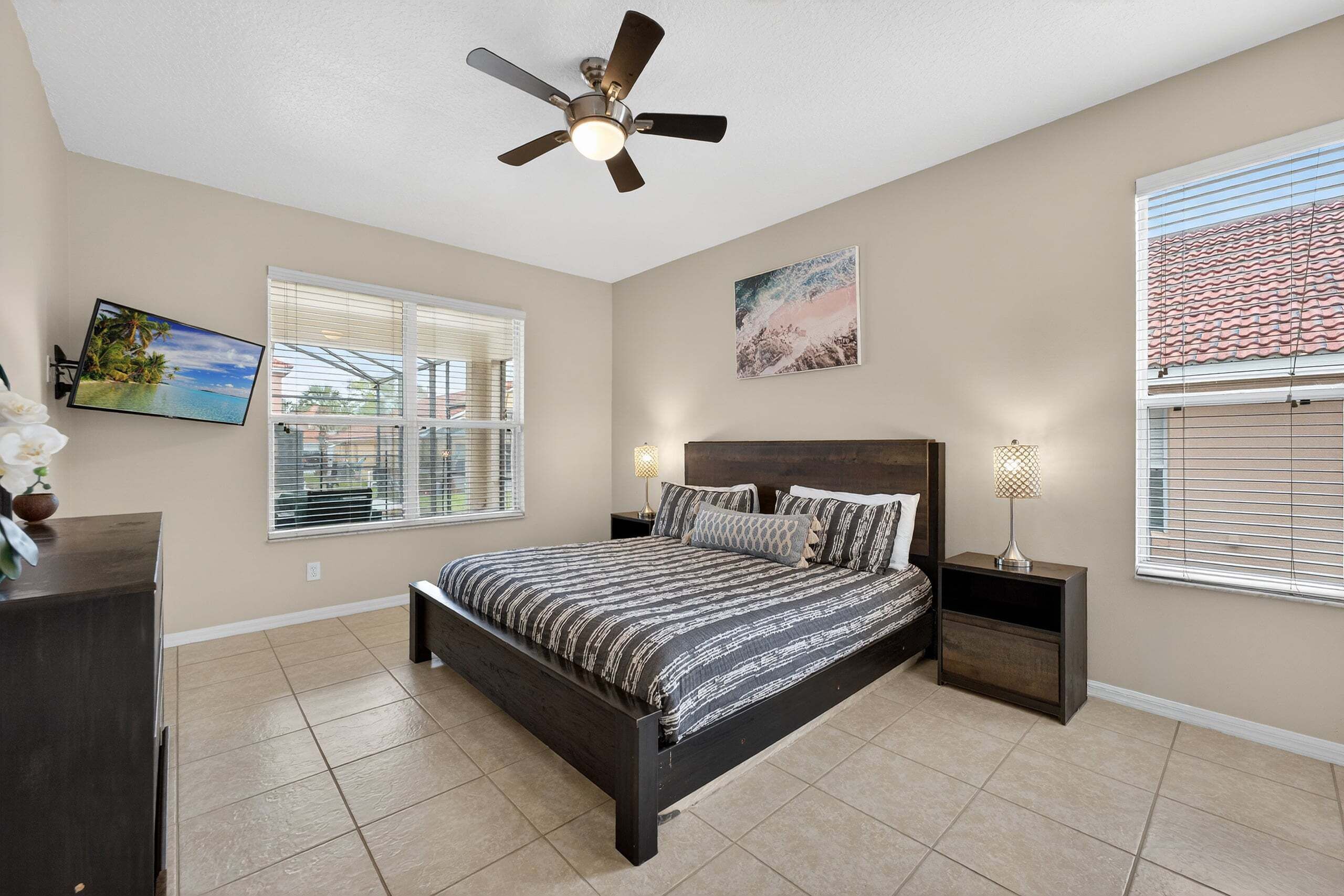 A bedroom with a bed, a ceiling fan, a TV, and a window with blinds.