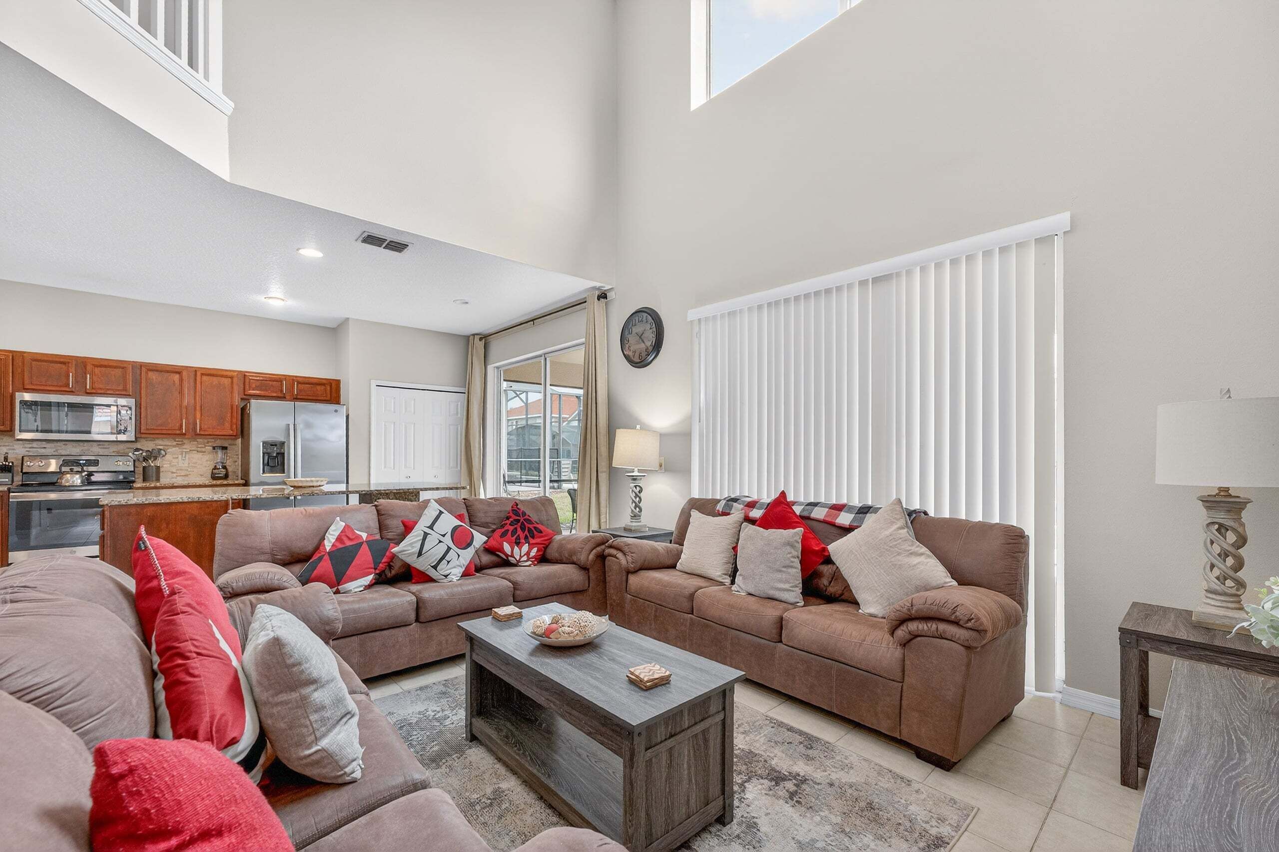 A spacious living room with a large brown sofa set, a coffee table, and a view of the kitchen and dining area.