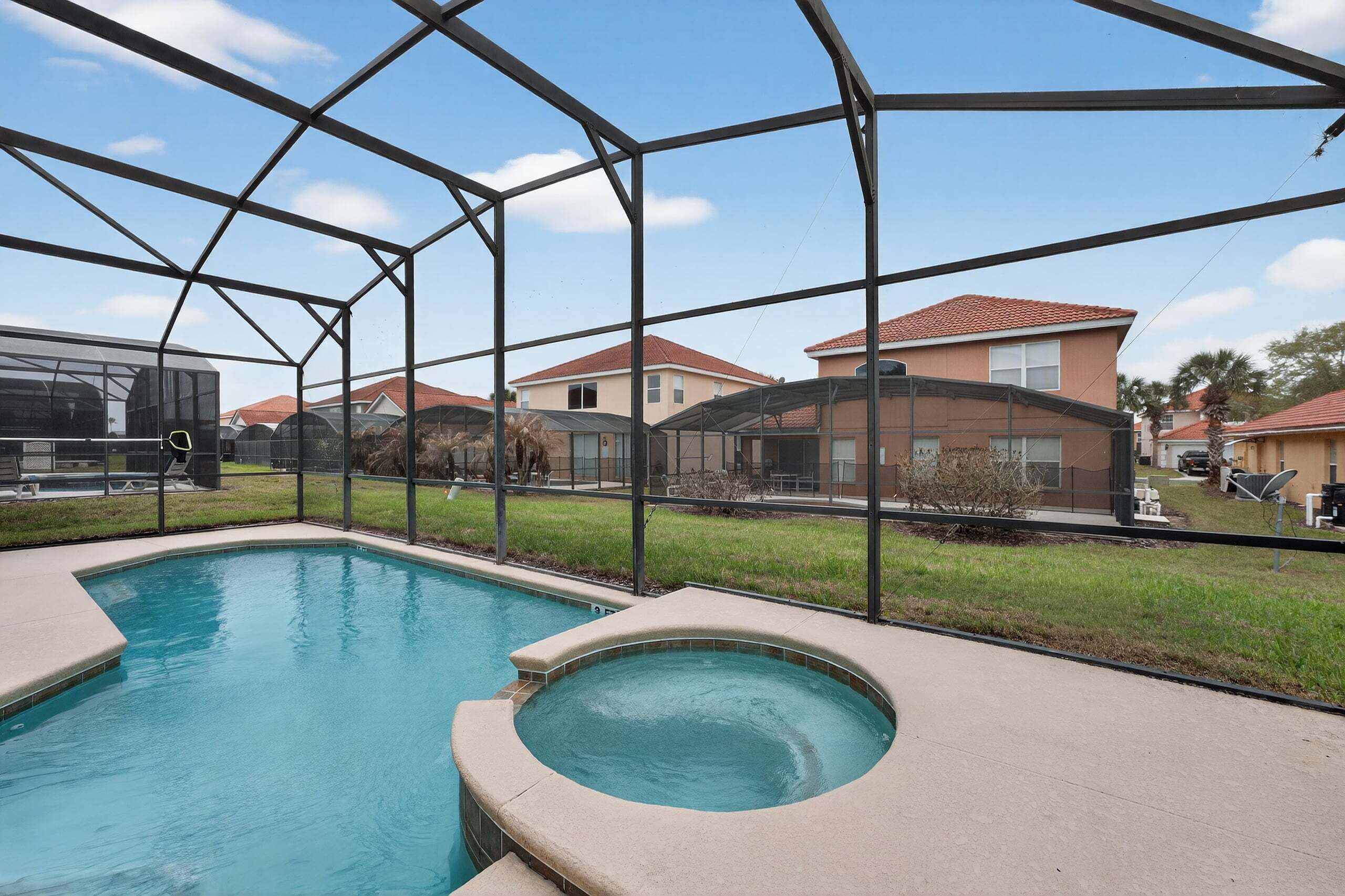 A swimming pool with a hot tub, surrounded by a metal fence, with houses in the background.