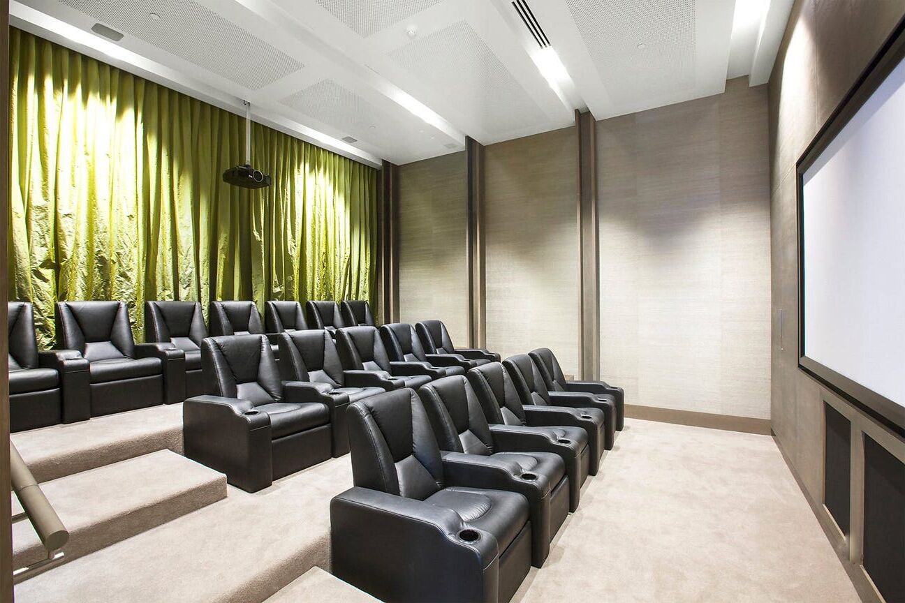 Ein Theaterraum mit Reihen schwarzer Ledersessel, einem grünen Vorhang und einer großen Leinwand.