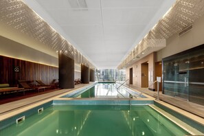 Ein moderner, überdachter Pool mit Blick auf die Stadtlandschaft, Liegestühlen und einer gemusterten Decke.