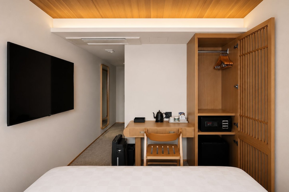 A hotel room with a bed, a desk, a chair, a wardrobe, a TV, and a mirror.