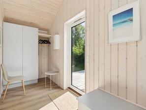 Una habitación con paredes de madera, una silla blanca, una mesita, un banco y una puerta que da al exterior.