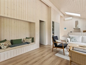 Una habitación amplia con suelo de madera, un sofá blanco, una mesa de comedor y un banco empotrado con cojines.