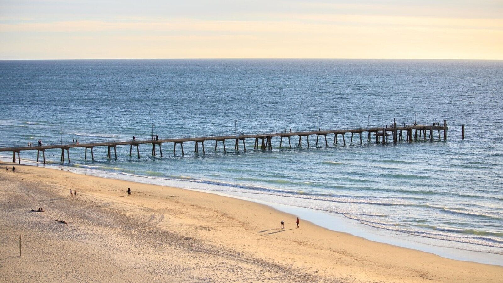 A beach with a wooden pier extending into the sea, sandy beach, and clear sky.